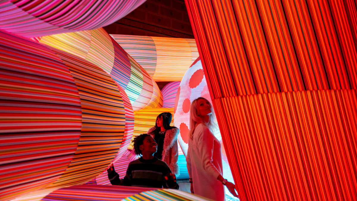 Personer går mellan stora mjuka figurer som lyser i olika färger